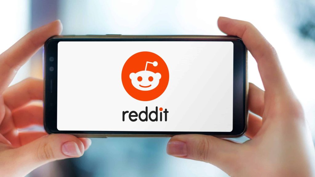 Mãos segurando um smartphone exibindo o logotipo do Reddit, um site americano de agregação de notícias sociais, classificação de conteúdo da web e discussão